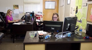 Two women work at desks in an office environment, focused on their computers.